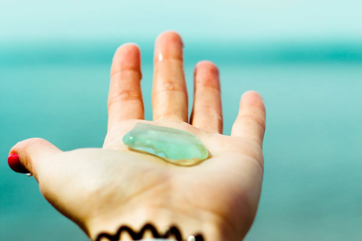 Piece of green frosted sea glass resting in an open hand by the sea