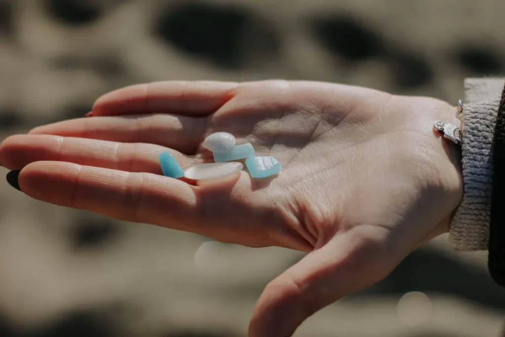 Hand holding several pieces of frosted sea glass above a sandy beach