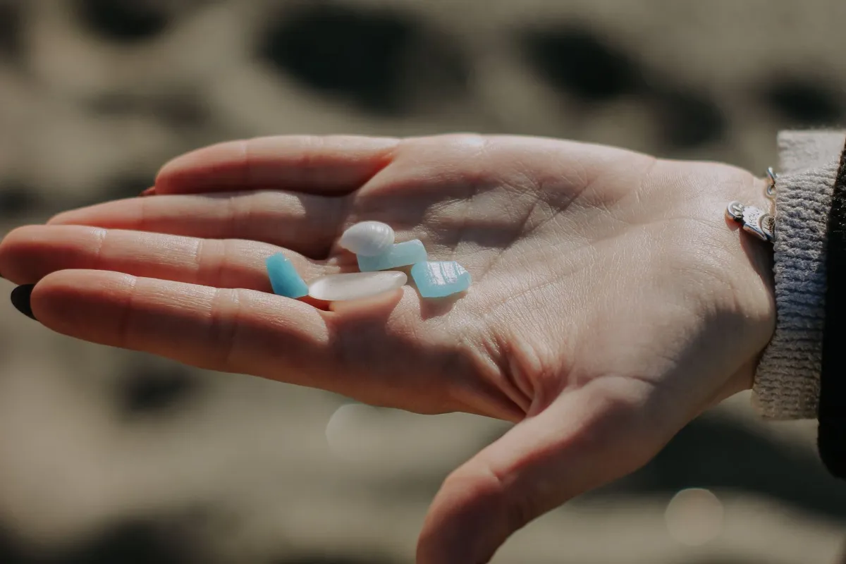 Hand holding several pieces of frosted sea glass above a sandy beach