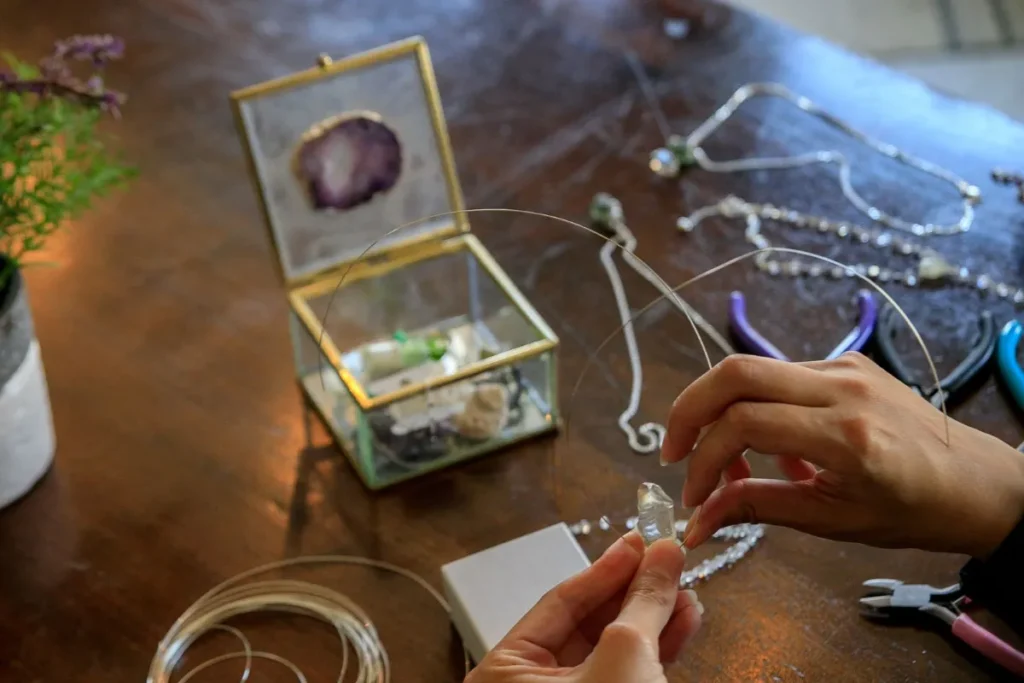 Hands making wire-wrapped jewelry at a table with pliers and stones