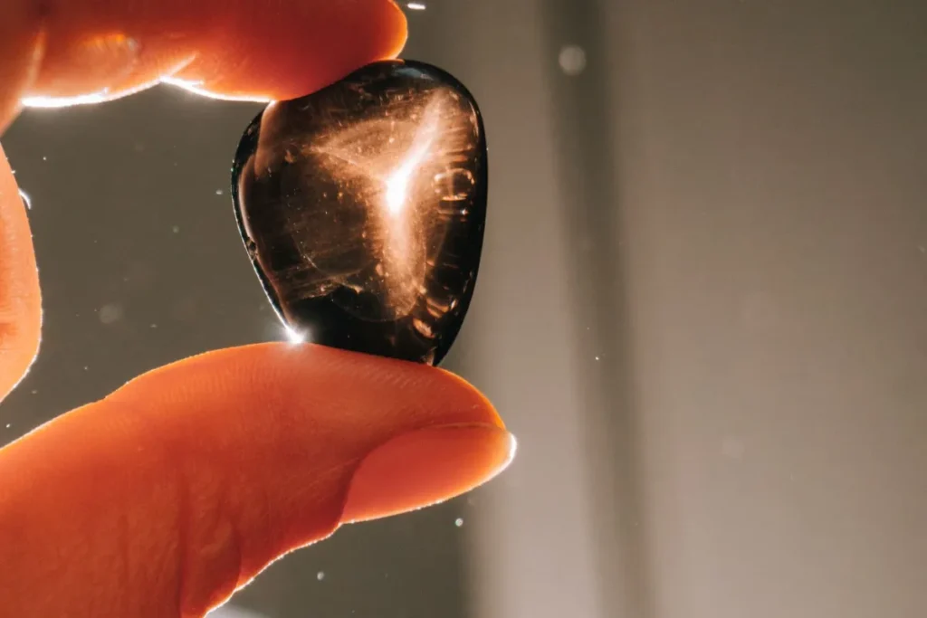 Polished black obsidian tumbled stone held up to the light